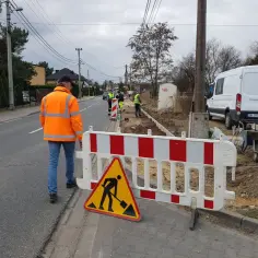 Ekipa remontowa pracuje przy drodze, ogrodzona barierami i znakiem ostrzegawczym.