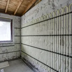 Instalacja ogrzewania ściennego wodnego w trakcie budowy. Jasne rurki ułożone pionowo i poziomo na ścianie z bloczków.