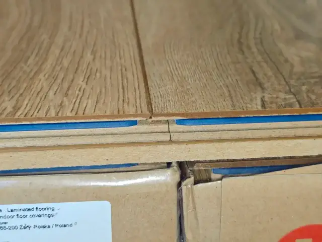 Zbliżenie na podłogę laminowaną z niebieską warstwą izolacyjną. Pokazuje, czy można położyć panele na panele, ukazując strukturę podłogi.
